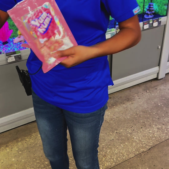 PetSmart employee in uniform holding a bag of Watermelon YumNums Freeze-Dried Candy, smiling while trying the crunchy, juicy watermelon snack for the first time in a taste-test video.